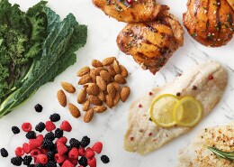 Cooked fish with lemon slices, berries, nuts, greens, grains, and chicken breast