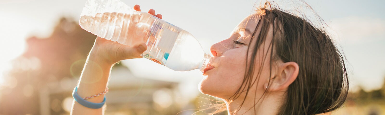 A young female drinking a bottle of water while standing outside