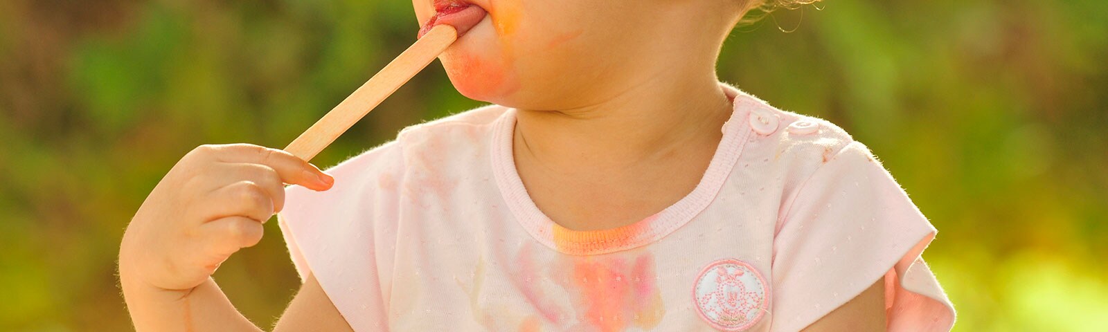 A young girl eating a melted popsicle with stains on her shirt A young girl eating a melted popsicle with stains on her shirt