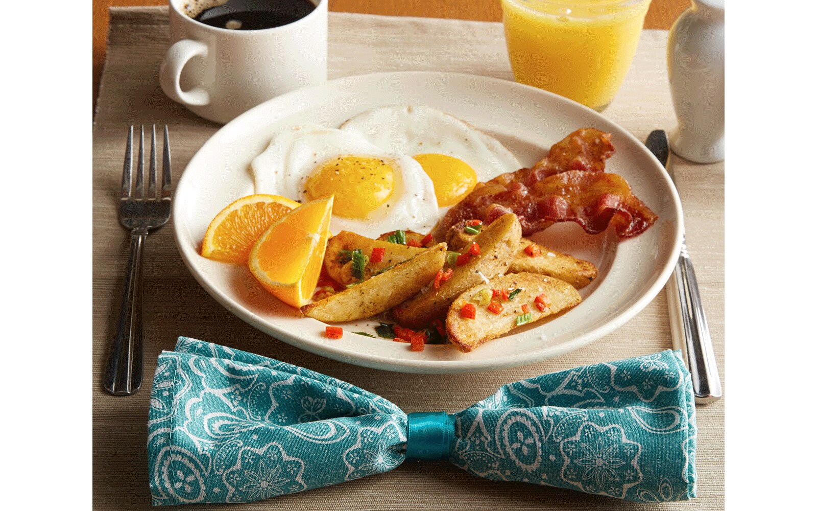 Breakfast including eggs and bacon on a plate with coffee and orange juice on a table