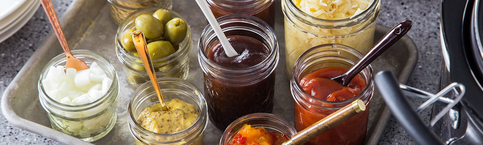 A bunch of condiments like ketchup, olives, BBQ sauce and sauerkraut on a metal tray A bunch of condiments like ketchup, olives, BBQ sauce and sauerkraut on a metal tray