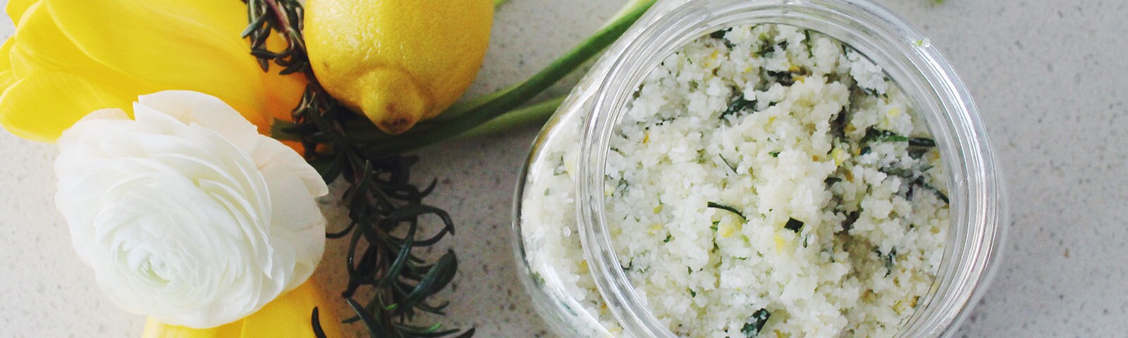Salt scrub in mason jar next to white rose and rosemary