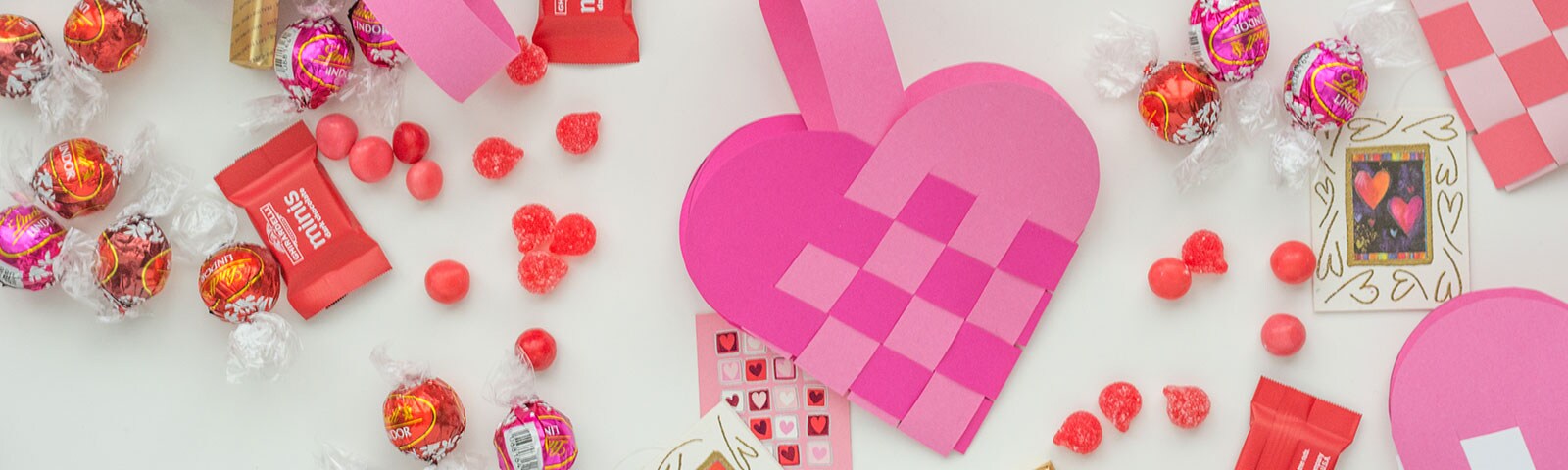Finished handmade woven heart treat bags in pink cardstock paper surrounded by candy Finished handmade woven heart treat bags in pink cardstock paper surrounded by candy