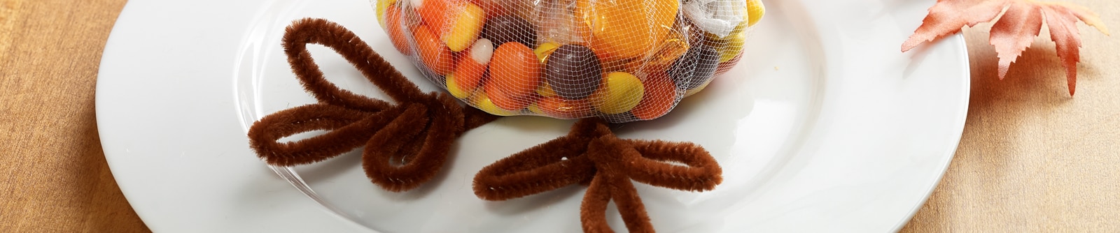 A bag of mixed candy with turkey legs made from brown pipe cleaners sit on a white plate