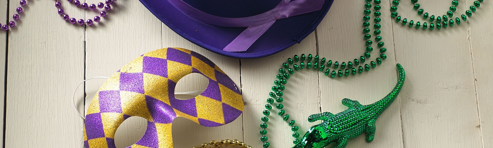 Mardi Gras beads, masks, and hats on a white painted wooden table