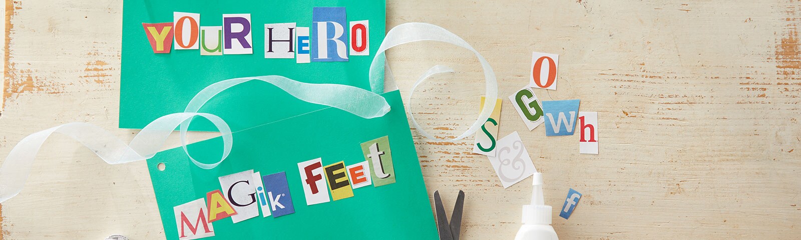 Two green cards on a wooden background, one says YOUR HERO using magazine clippings and the other say MAGIK FEET Two green cards on a wooden background, one says YOUR HERO using magazine clippings and the other say MAGIK FEET