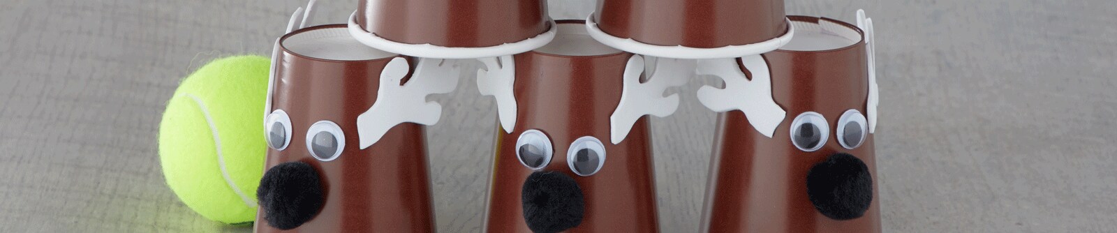 A stack of DIY reindeer using brown plastic cups with googly eyes, felt antlers and pompoms next to a tennis ball A stack of DIY reindeer using brown plastic cups with googly eyes, felt antlers and pompoms next to a tennis ball