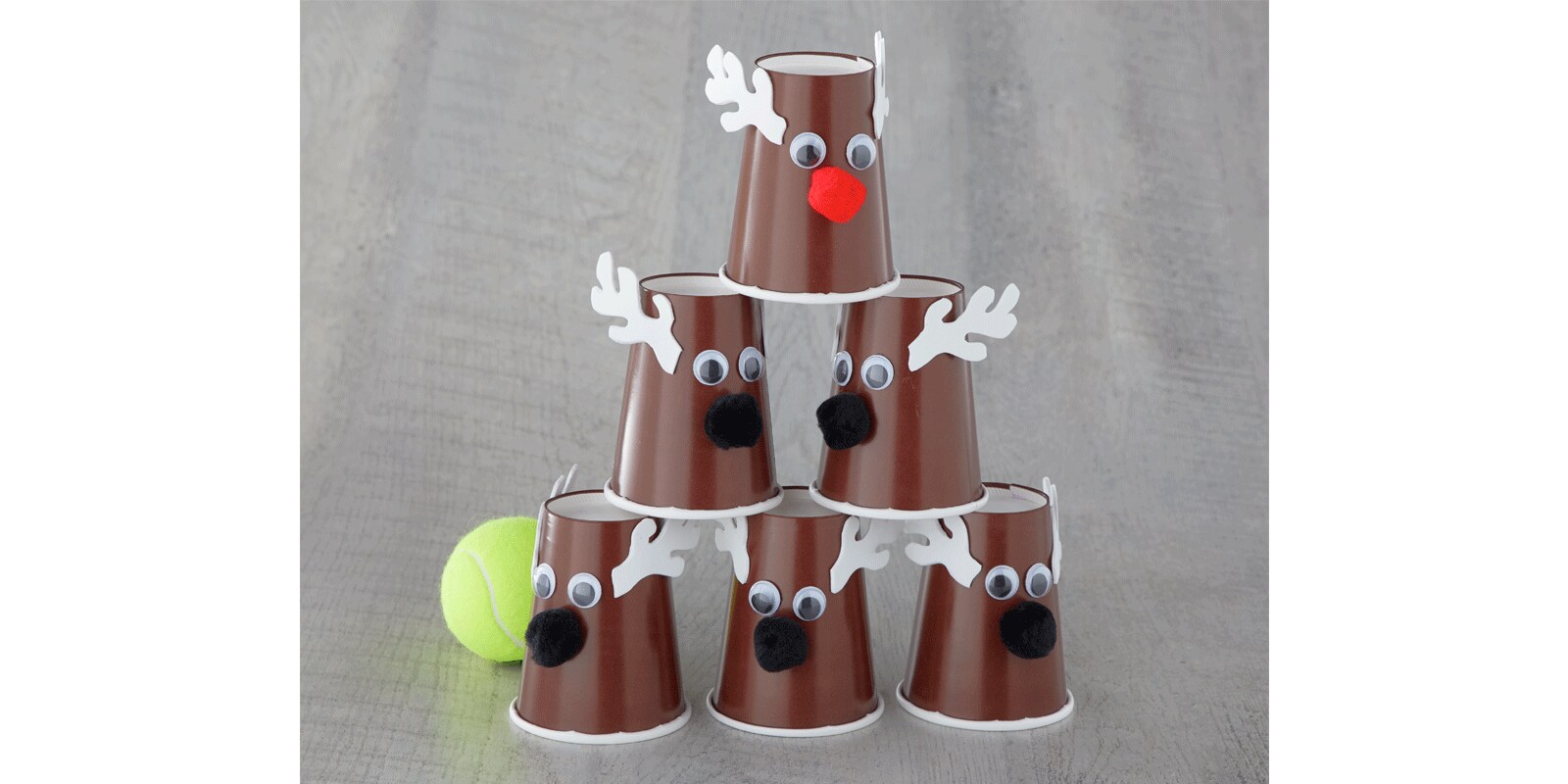A stack of DIY reindeer using brown plastic cups with googly eyes, felt antlers and pompoms next to a tennis ball A stack of DIY reindeer using brown plastic cups with googly eyes, felt antlers and pompoms next to a tennis ball